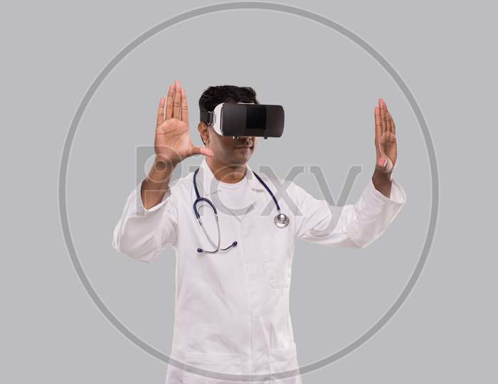 Doctor Wearing Vr Glasses Hands To Sides Isolated. Indian Man Doctor Pointing In Virtual Reality