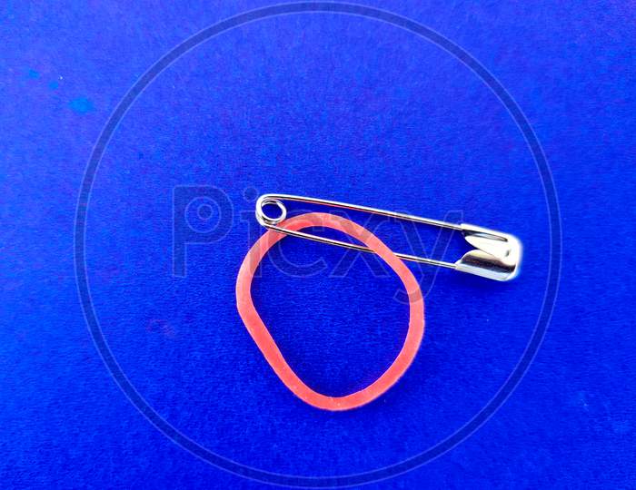 Safety Pin And Red Color Rubber Band On Blue Background. Selective Focus