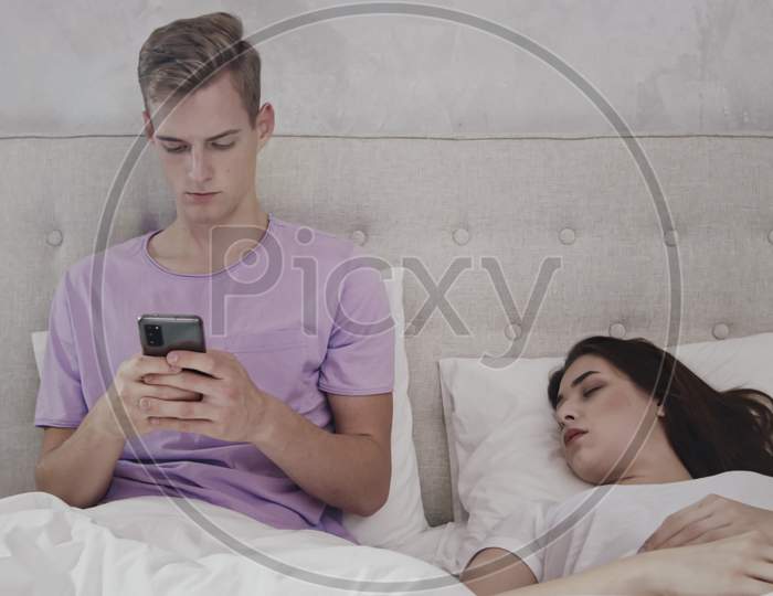 Man Chatting On Phone While Girl Is Sleeping. Man Using Phone In Bed. Girl Sleeping In Bed. Shot On Red