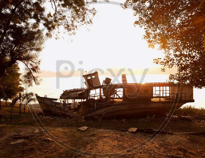 Boat wreckage beside a river in the glowing morning.