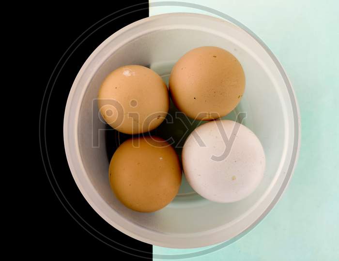 Top View Of Three Brown Eggs And One White Egg In White Plastic Box. Isolated On Black And Mint Color Background.