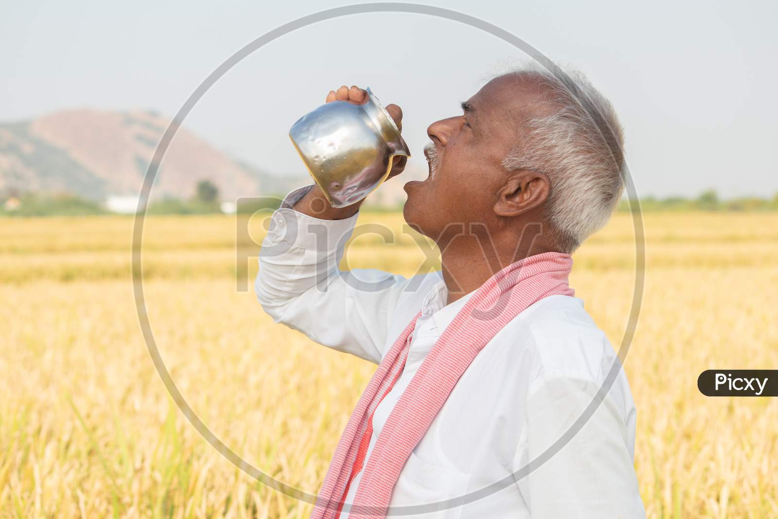 Thirsty Indian Farmer Drinking Water From Steel Tumbler Or Chambu On Hot Sunny Day At Agriculture Field
