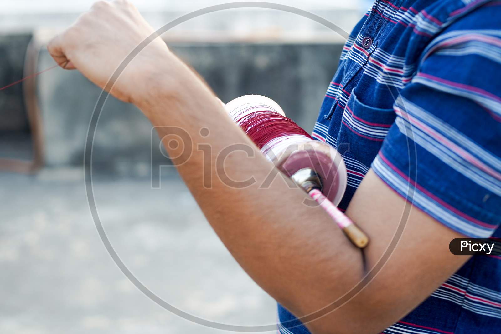 Man Holding A Charki Phirki Thread Spool In The Crook Of His Elbow And Winding It With The Other Hand To Ensure Taughtness For The Famed Kite Fighting Festival Of Makar Sankranti Uttarayana