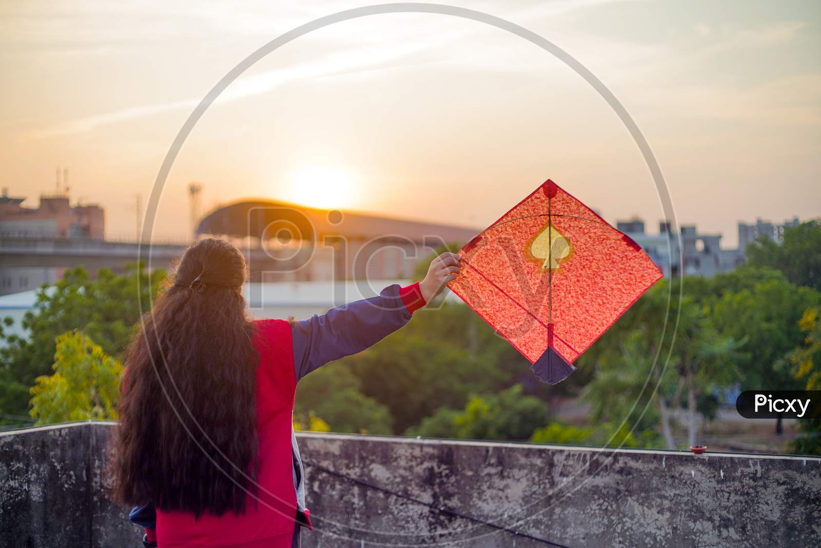 Young Woman Holding Aloft Colorful Paper And Wood Kite Against A Blurred Background Setting Sun On The Indian Kite Festival Of Makar Sankranti Or Uttarayana