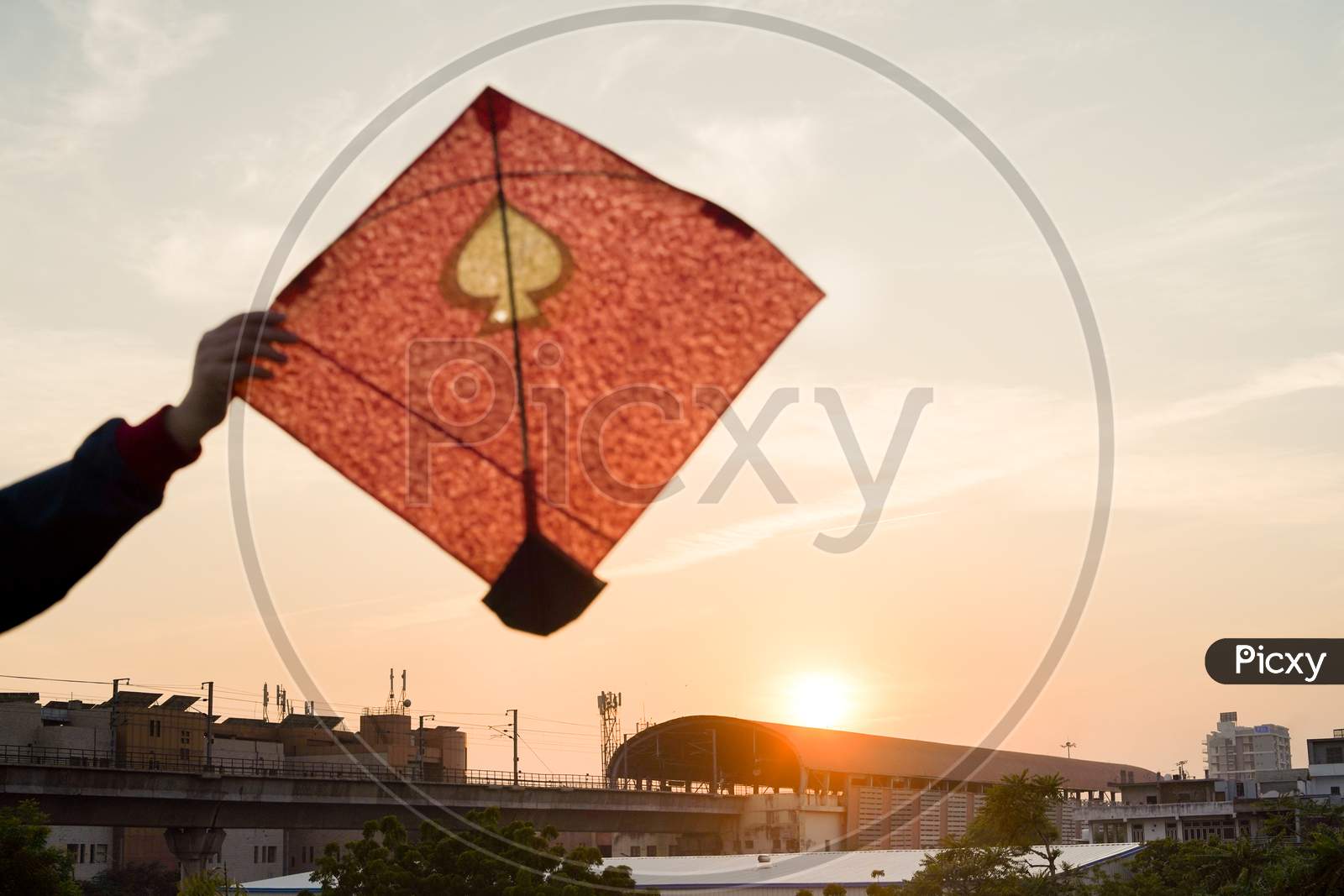 Young Man Holding Aloft Colorful Paper And Wood Kite Against A Blurred Background Setting Sun On The Indian Kite Festival Of Makar Sankranti Or Uttarayana