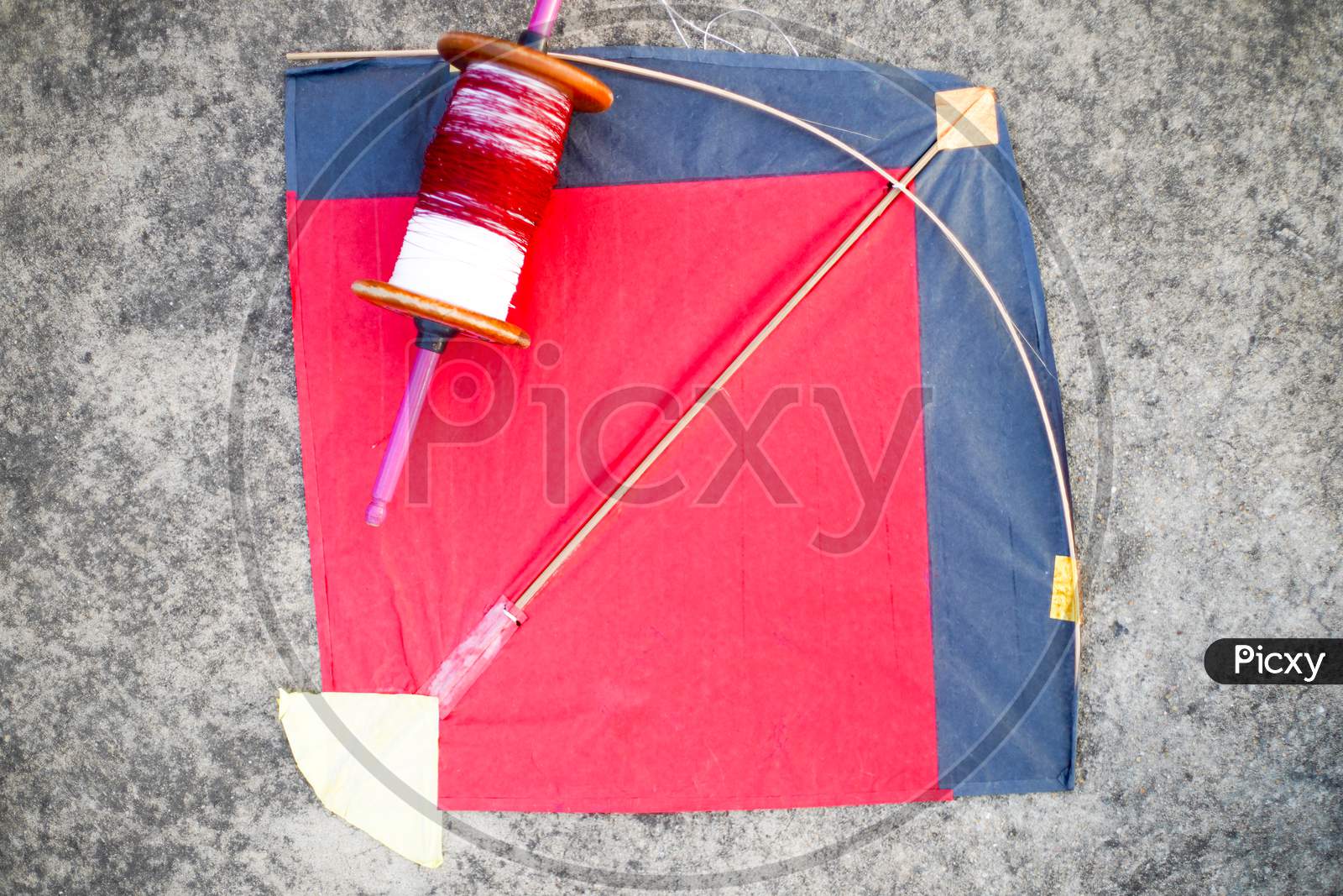 Top Down Flatlay Shot With Red And Black Paper And Wood Kite With A Wooden Handmade Charkhi Thread Spool With Normal And Glass Covered Thread For Kite Fighting On Teh Indian Festival Of Makar Sankranti Uttarayana