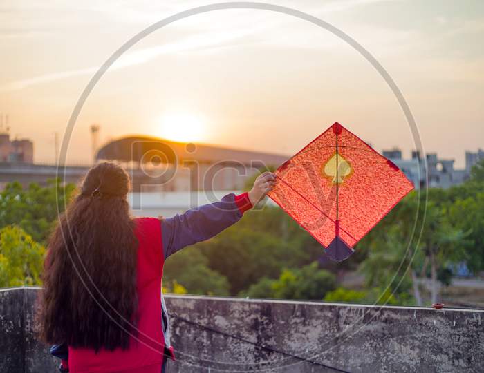 Young Woman Holding Aloft Colorful Paper And Wood Kite Against A Blurred Background Setting Sun On The Indian Kite Festival Of Makar Sankranti Or Uttarayana