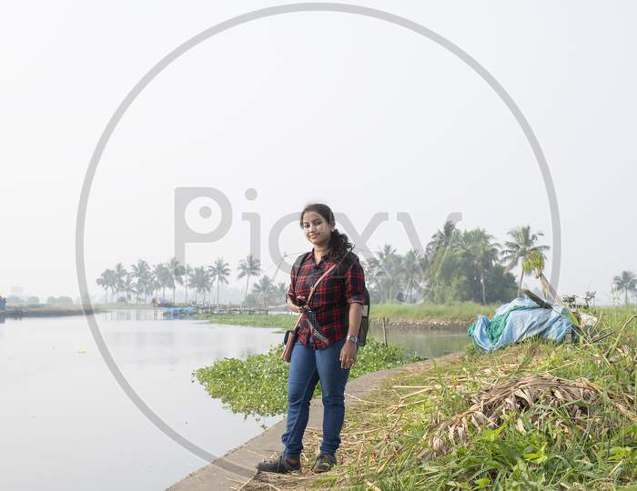 women's day ,women entrepreneur, A Kerala Women Explorer With Backpack On Village Road Next To A River Surrounded By Green Grass On White Blur Smoky Background From Kadamakudy Kerala India. The Natural Beauty Of This Place Is Amazing