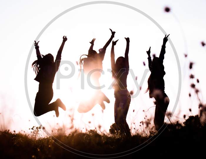 Girls Jump Together Against The Sky At Top Of The Mountain.