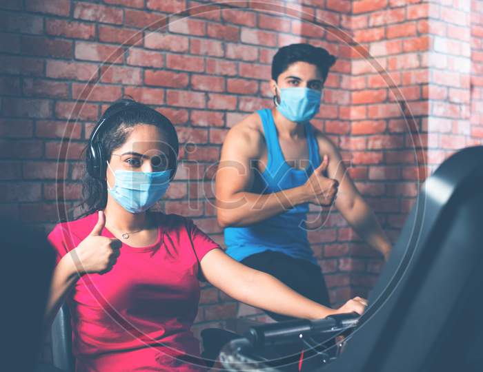Indian Young Couple Wears Face Mask While Riding On Fitness Bike In The Gym