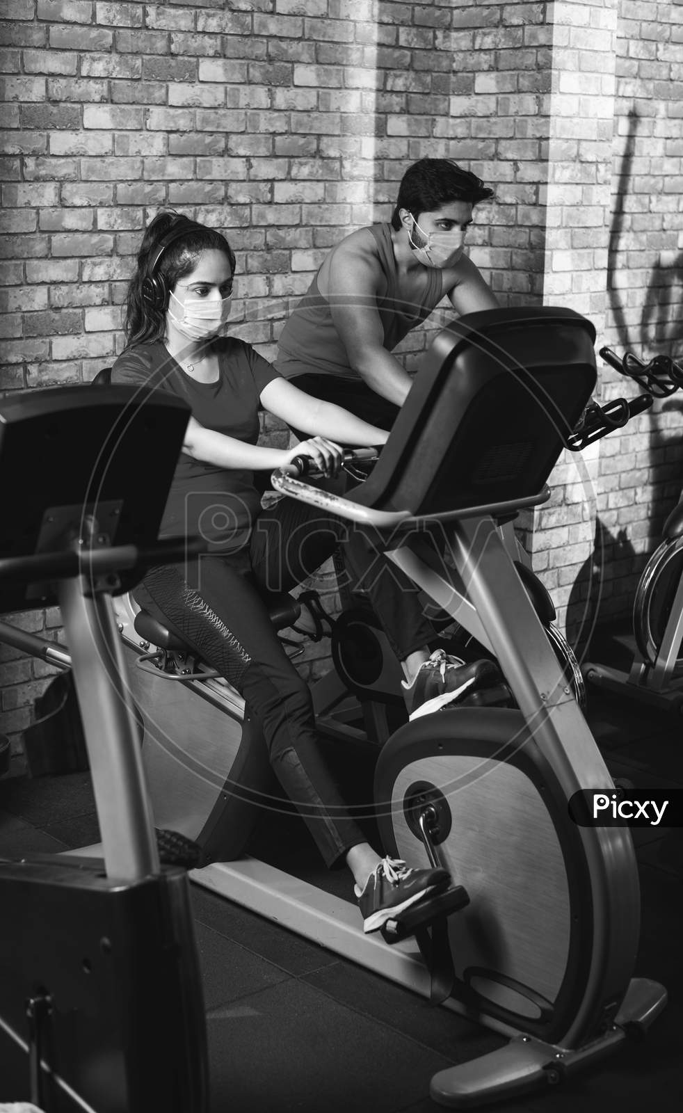 Image of Indian Young Couple Wears Face Mask While Riding On Fitness Bike  In The Gym-GH749305-Picxy