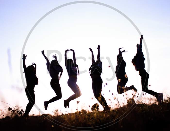 Girls Jump Together Against The Sky At Top Of The Mountain.