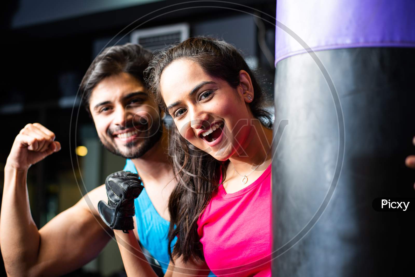 Portrait Of Indian Asian Young Couple Working Out Together In Gym With Punching Bag