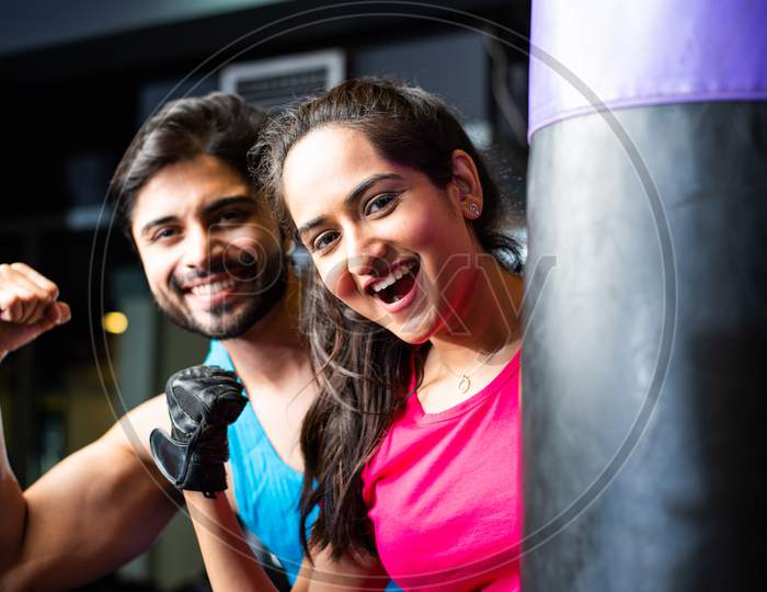 Portrait Of Indian Asian Young Couple Working Out Together In Gym With Punching Bag