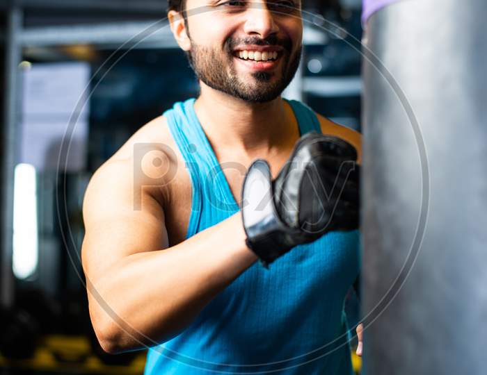 Indian Man Punching With Gloves On Sand Bag, Asian Boxer In Gym