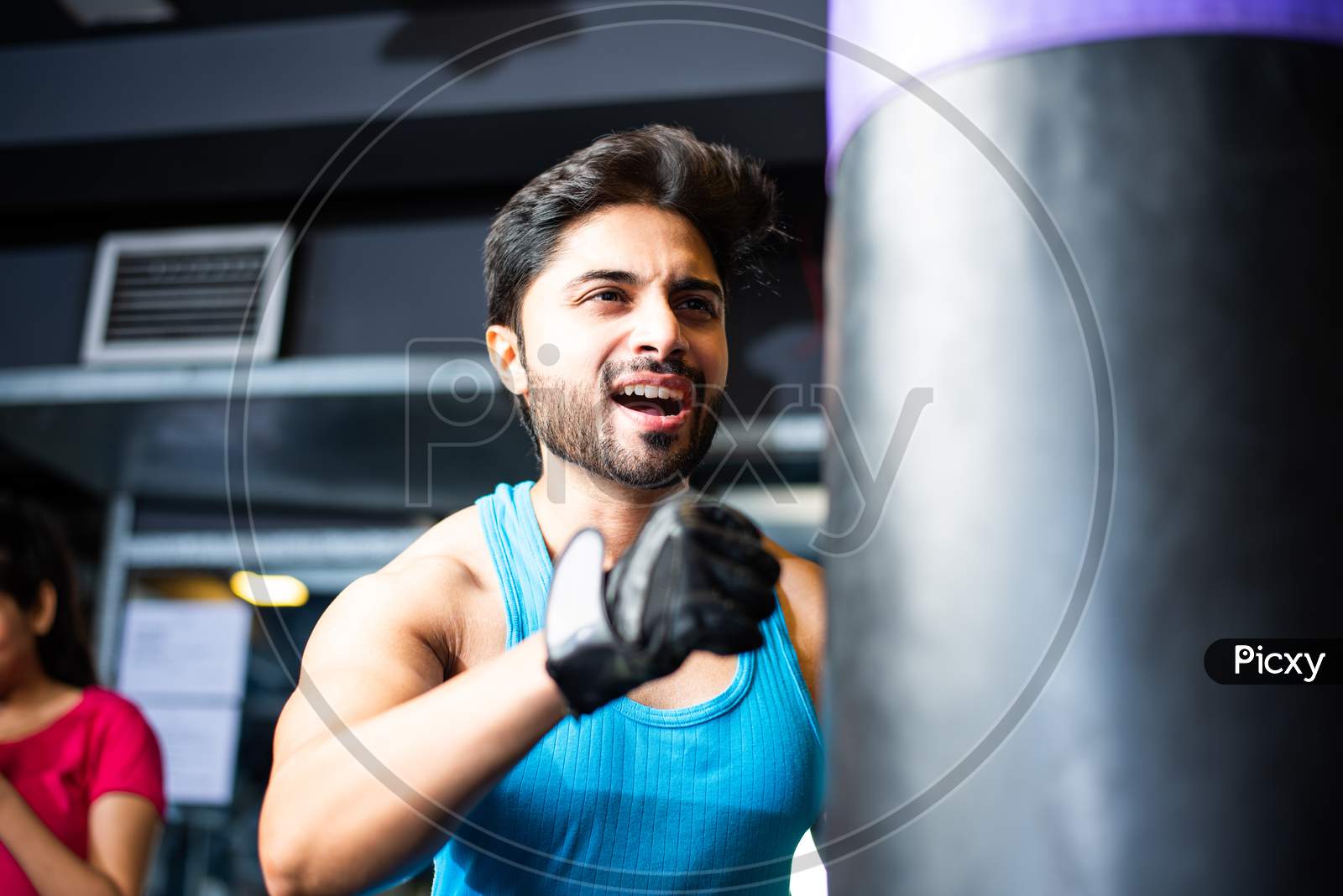 Indian Man Punching With Gloves On Sand Bag, Asian Boxer In Gym