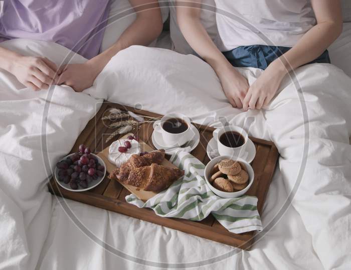 Couple Having Breakfast In Bed. Couple Eating In Bed. Man Taking Cookie, Girl Taking Grape. Food Close Up. Tea And Coffee Cups. Shot On Red