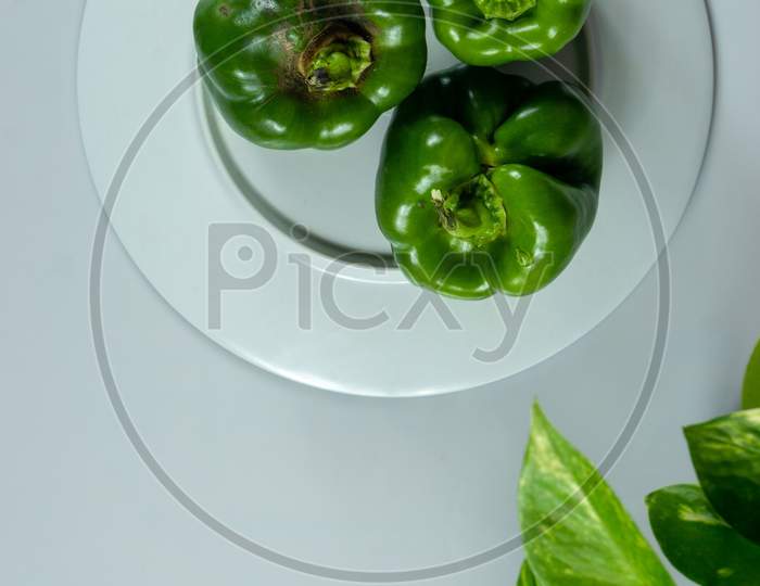Fresh Green Capsicum Placed On A Plate With White Background