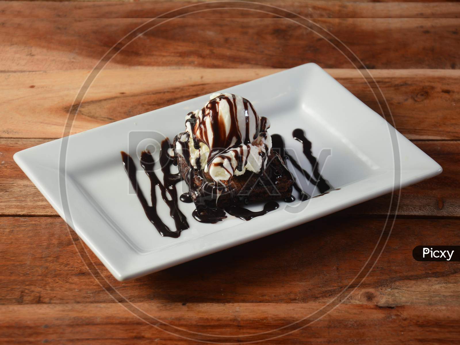 Brownie Sundae With A Scoop Of Vanilla Ice Cream, Chocolate Sauce, Whipped Cream On White Plate