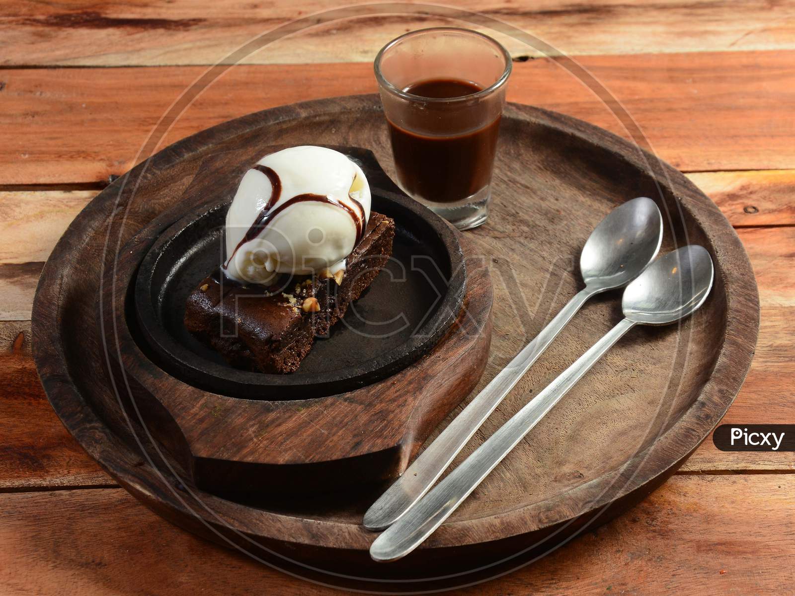 Sizzling Chocolate Brownie Is A Sweet Dish Made Using Scoop Of Ice-Cream On Top Served With A Generous Pouring Of Melted Chocolate Syrup On Wooden Plate. Server Hot. Selective Focus