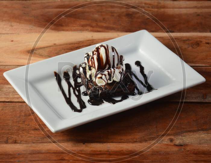 Brownie Sundae With A Scoop Of Vanilla Ice Cream, Chocolate Sauce, Whipped Cream On White Plate