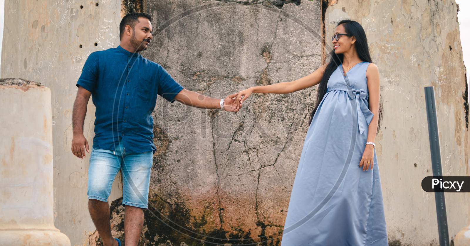 Two Beautiful Models, A Young Married Couple, Mother To Be Pregnant Lady, Holding Hands, And Looking At Each Other Standing Against An Old Wall, Portraiture In Front Of Ruins Of Galle Dutch Fort.
