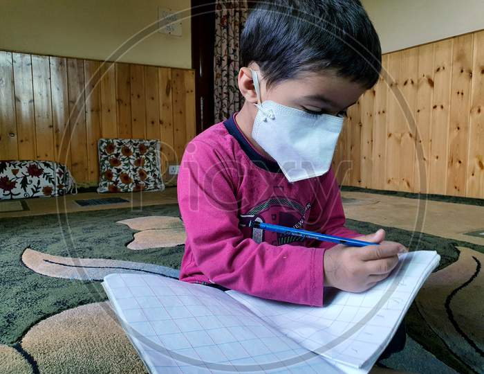 Masked Students  Reading And Writing Their School Work At Home During The Pandemic Coronavirus. Online Classes Are Common Due To Covid 19.