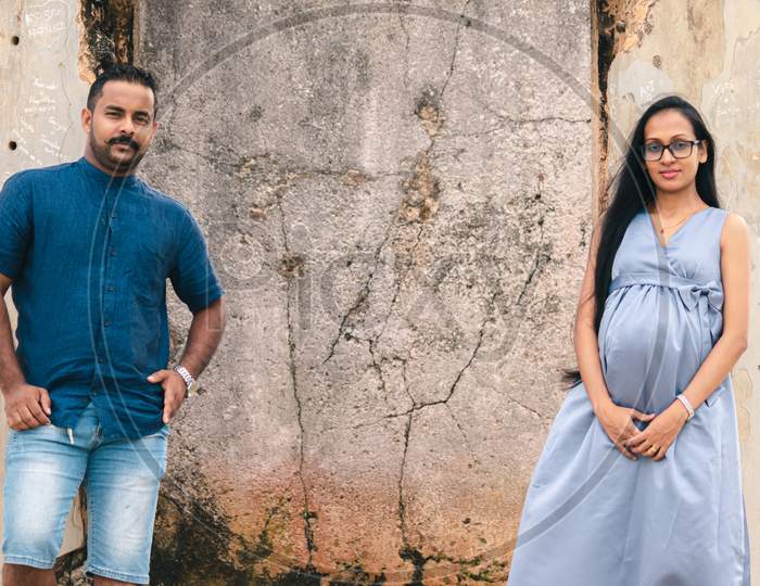 Two Beautiful Models, A Young Married Couple, Mother To Be Pregnant Lady, Holding Hands, And Looking At Each Other Standing Against An Old Wall, Portraiture In Front Of Ruins Of Galle Dutch Fort.