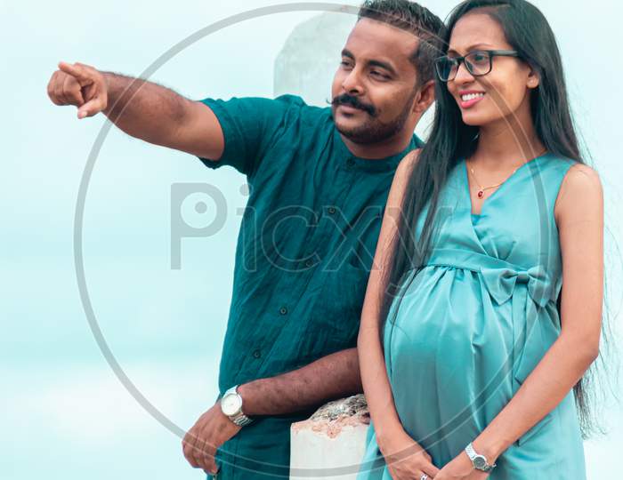 A Young Couple, Husband Pointing At Something In The Distance, A Beautiful Pregnant Lady With A Cute Smile, Standing Portrait In Natural Light, And Great Weather Conditions In Galle Fort.