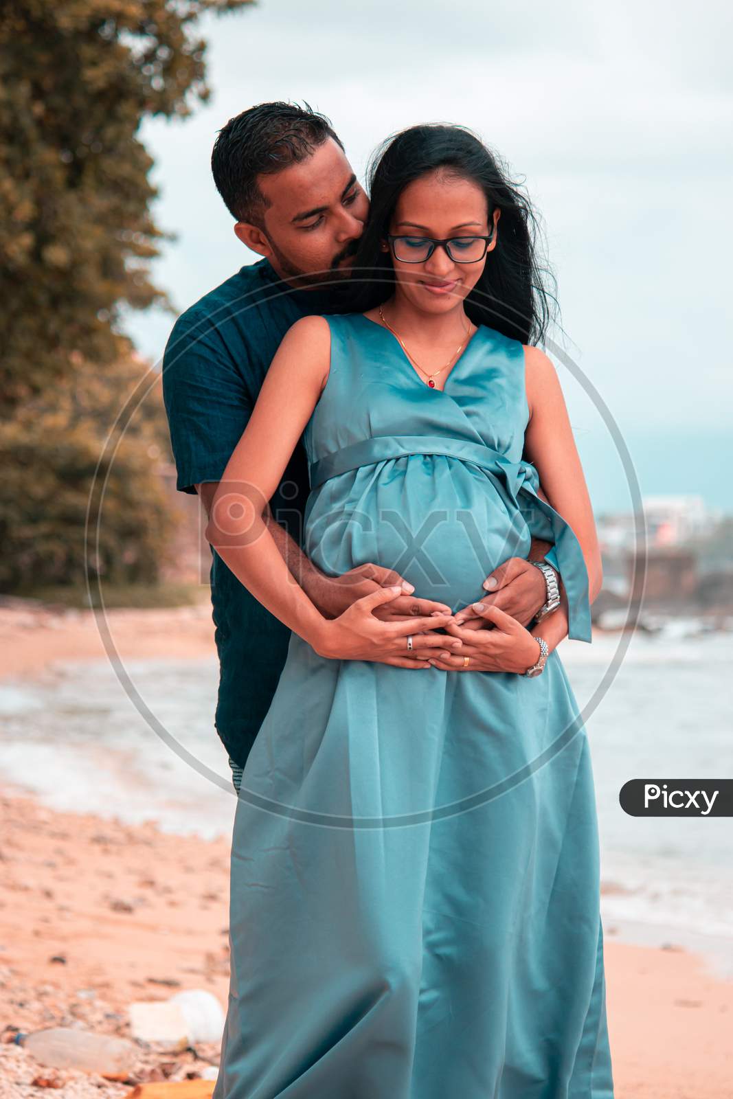 Young Parents Expecting New Baby Holding Mother'S Tummy In Both Hands And Gentle Kiss In The Necks, Front Close Up Photograph Under Natural Lights In The Beach Of Galle.