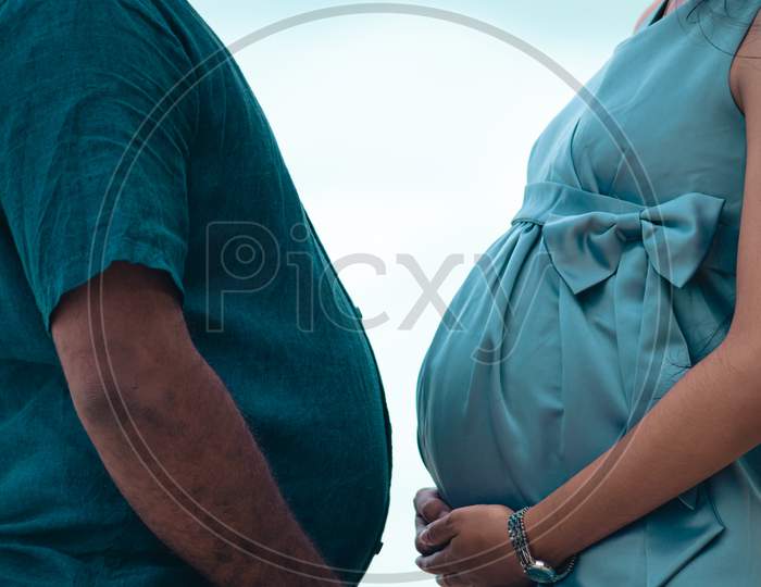 Pregnant Belly And A Beer Belly Against Each Other Together Close Up, Holding Bellies By Both Hands Side View, Couple Goals Concept.