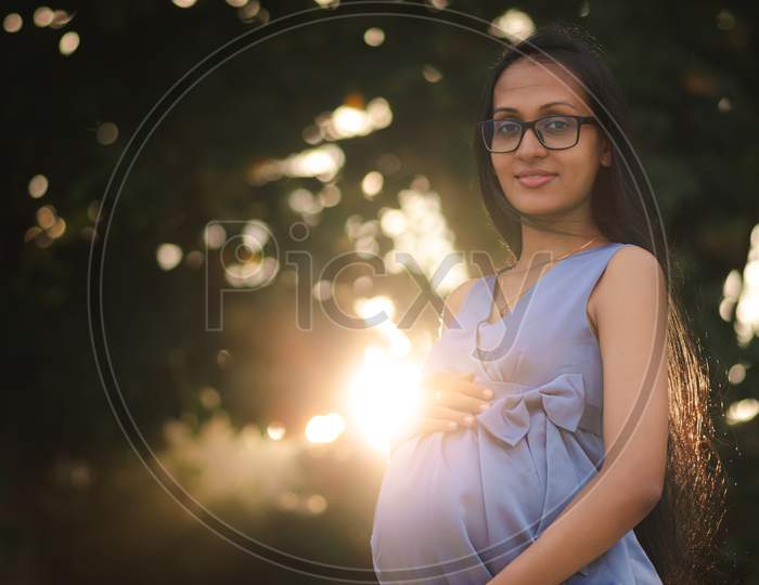 Young Beautiful Asian Pregnant Women With Glasses, Sun Is Rising Behind Her Belly Suggesting A New Life, Happy And Great Future Ahead Concept.