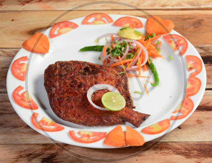 Pomfret Fish Fry - Deeply Fried Pomfret Fishes Which Is Well Garnished With Tomato, Lemon And Onion In A White Ceramic Plate With Wooden Background,Selective Focus