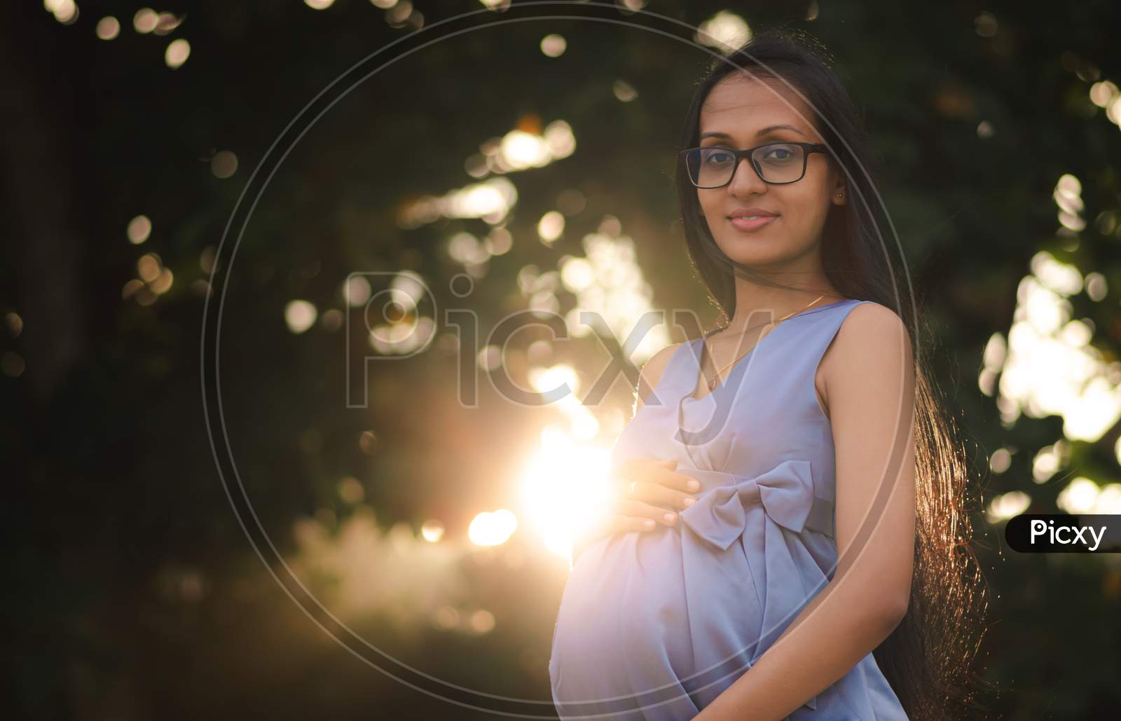 Young Beautiful Asian Pregnant Women With Glasses, Sun Is Rising Behind Her Belly Suggesting A New Life, Happy And Great Future Ahead Concept.