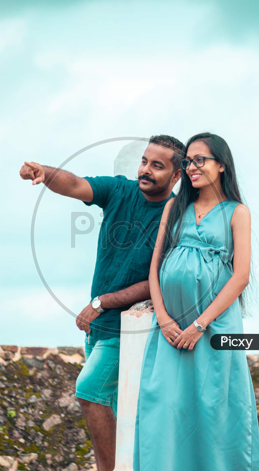 A Young Couple, Husband Pointing At Something In The Distance, A Beautiful Pregnant Lady With A Cute Smile, Standing Portrait In Natural Light, And Great Weather Conditions In Galle Fort.