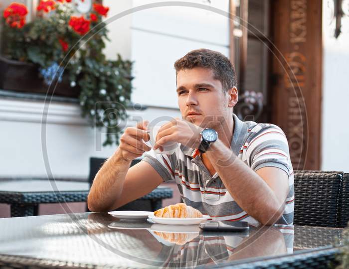 Young Man Drinking Coffee With Croissant