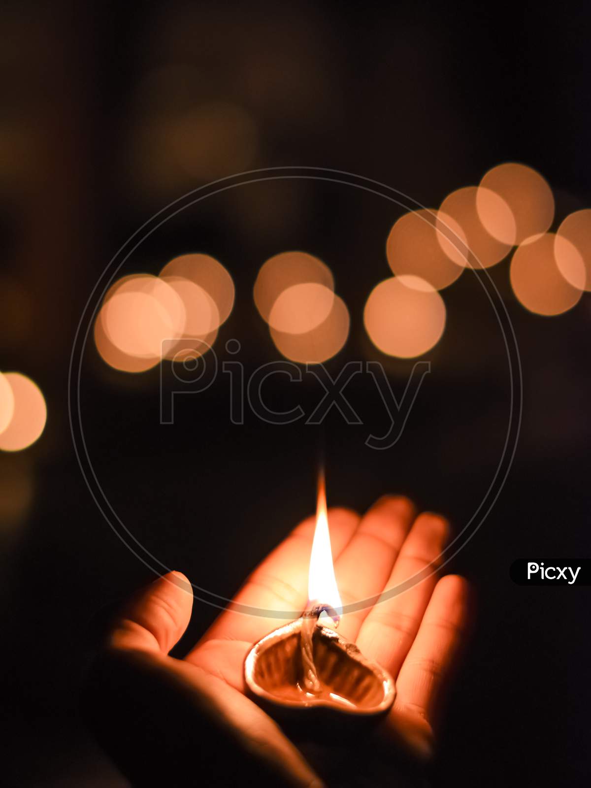 Portrait Photo Taken During Diwali Festival Night Of The Lit Clay Diya Oil Lamp Held In The Hand With Orange Light Bokeh As Background.