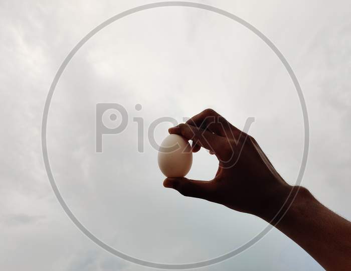 Hand Holding An White Egg In Clouds/Sky Background.