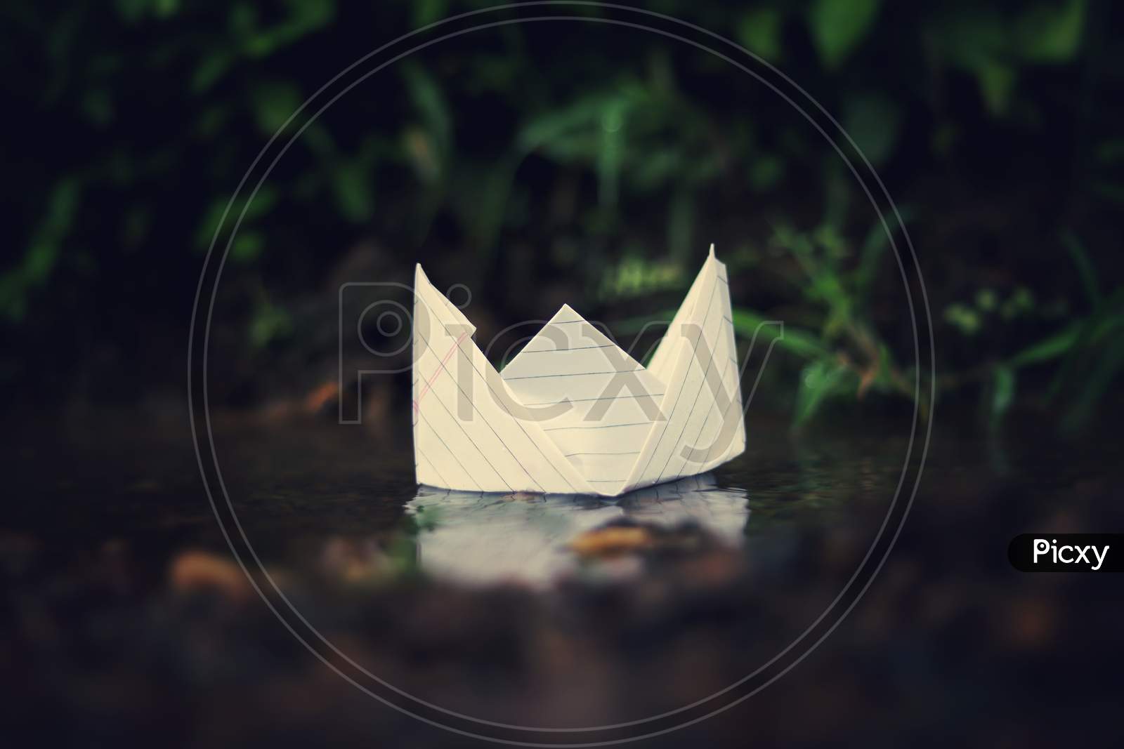 A small paper boat floating in the rainy water in rainy season with green nature background