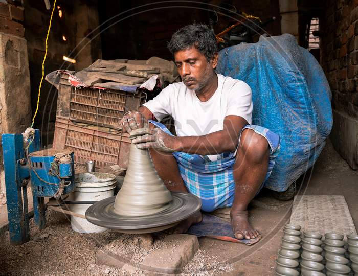 Indian Potter Making Small Pot Or Diya For Diwali With Clay On Potters Wheel In His Small Factory.Handwork Craft.