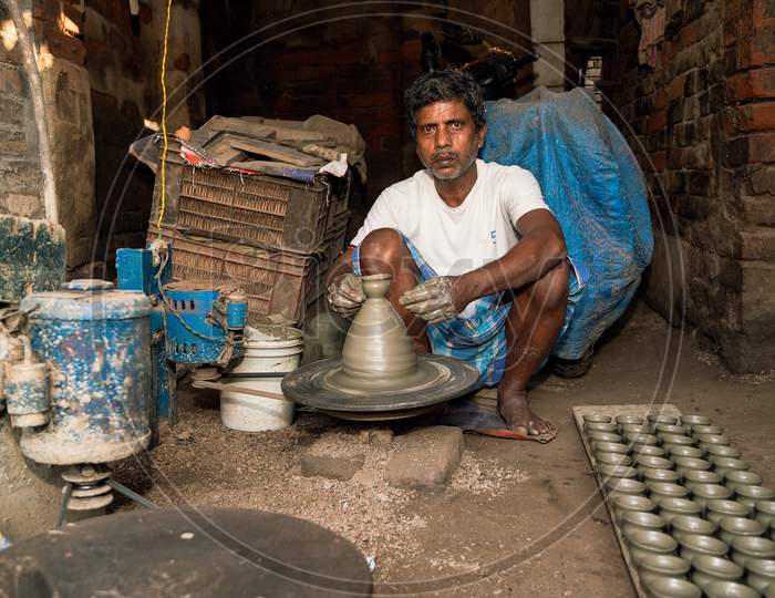 Indian Potter Making Small Pot Or Diya For Diwali With Clay On Potters Wheel In His Small Factory. Manufacturing Traditional Handicraft With Clay.