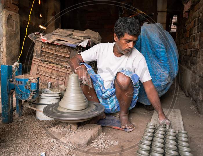 Indian Potter Making Small Pot Or Diya For Diwali With Clay On Potters Wheel In His Small Factory. Manufacturing Traditional Handicraft With Clay.