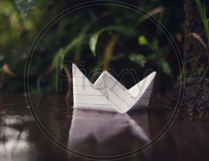 A small paper boat floating in rainy water in rainy season with nature background