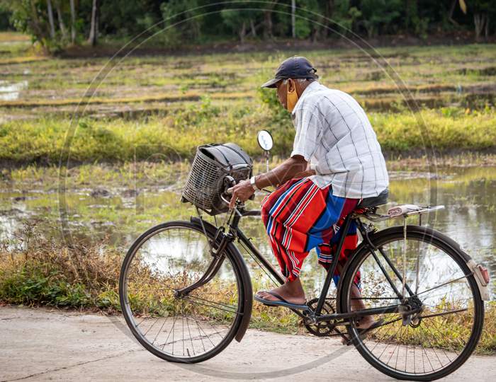 Galle, Southern Province / Sri Lanka - 10 24 2020: Old Grandpa With Face Mask Ride A Bicycle Near A Rice Paddy Field In A Rural Village In Galle.