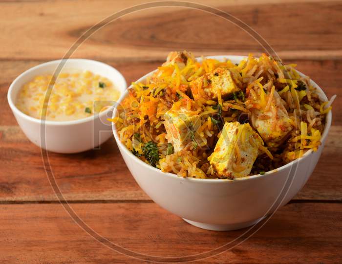 Hyderabadi Veg Paneer Dum Biryani With Mixed Veggies Like Paneer, Potato, Carrots, Peas Cooked Along With Spiced Rice And Served With Onion Raita And Curry, Selective Focus