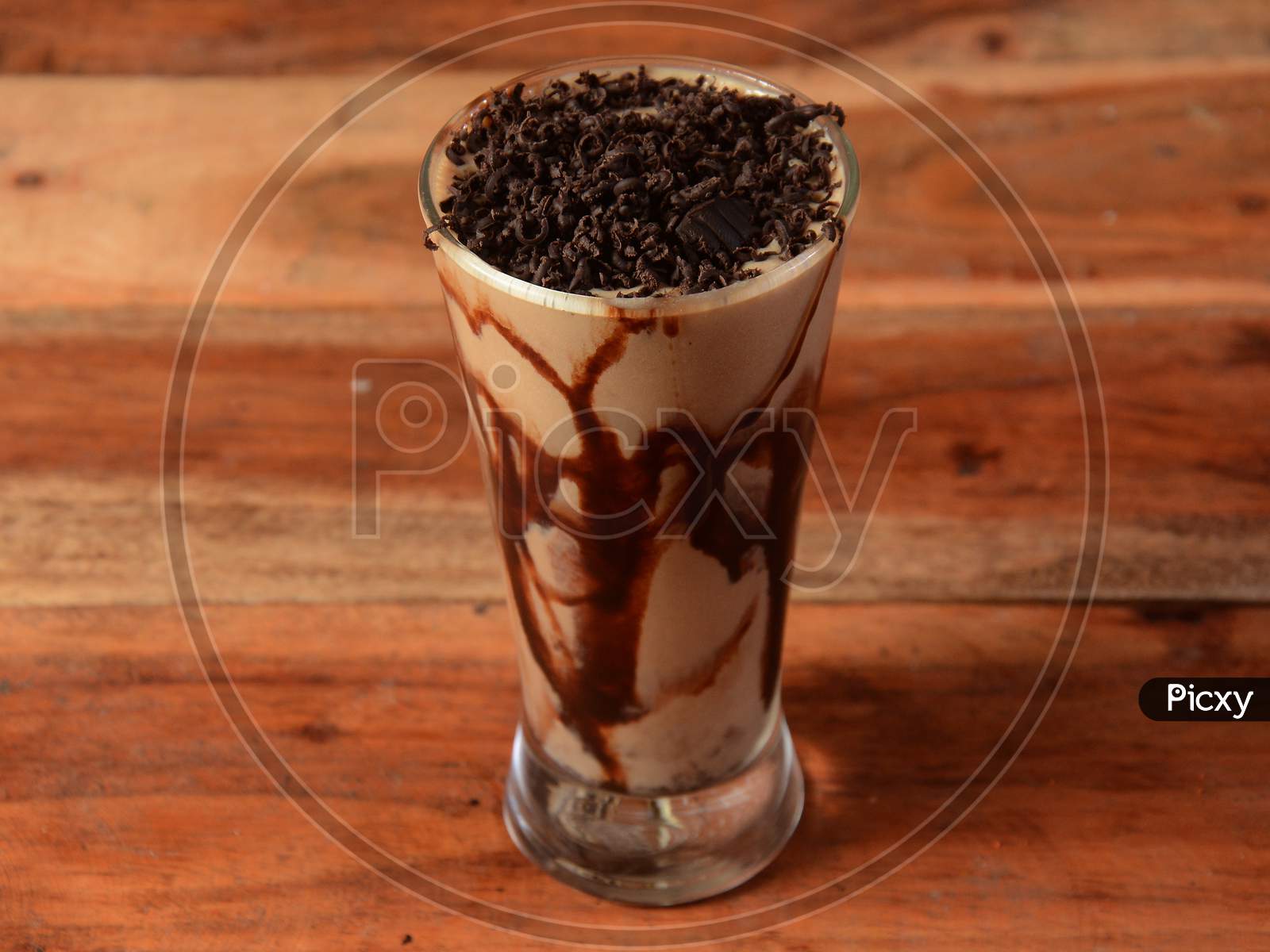 Cold Coffee In A Tall Glass With Chocolate Crushes Poured On A Old Rustic Wooden Table.