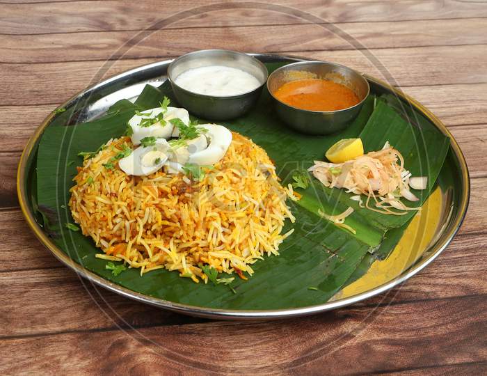 Aromatic Delicious Egg Biryani - Basmati Rice Cooked With Masala Spices And Served With Along With Sliced Boiled Egg, Gravy, Onion Raita And Green Salad Served On Banana Leaf With Plate, Selective Focus