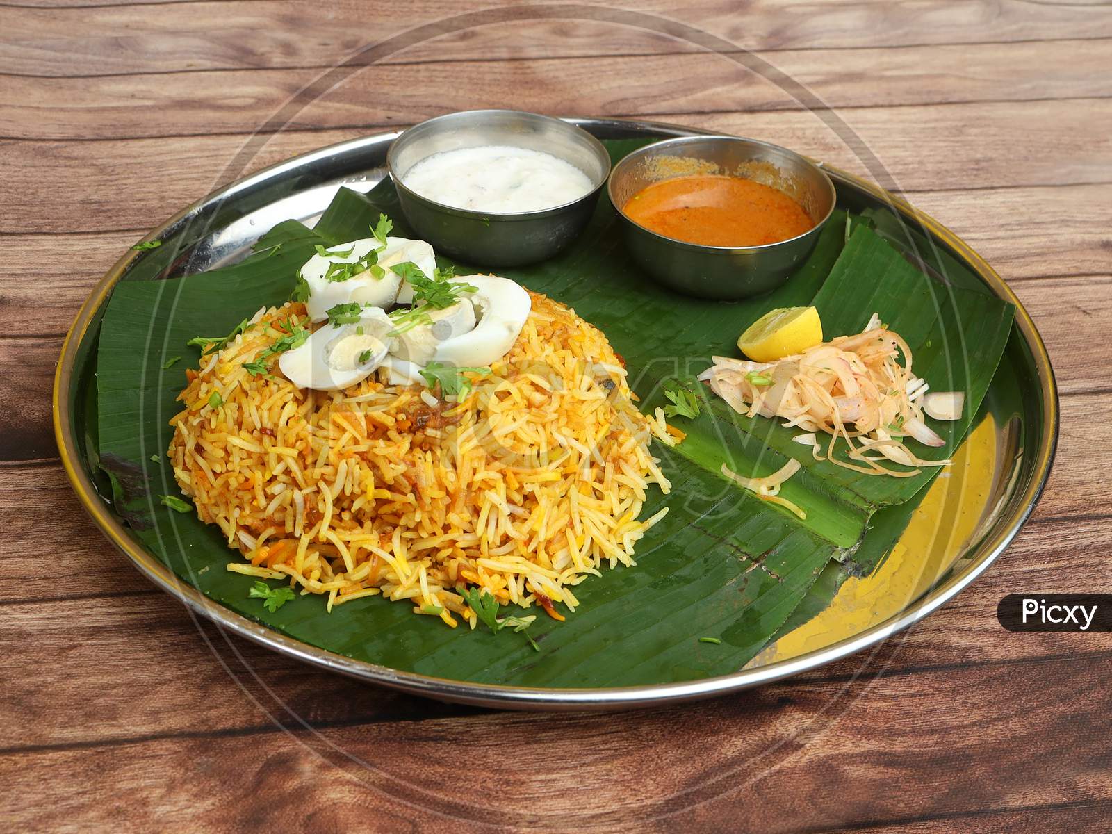 Aromatic Delicious Egg Biryani - Basmati Rice Cooked With Masala Spices And Served With Along With Sliced Boiled Egg, Gravy, Onion Raita And Green Salad Served On Banana Leaf With Plate, Selective Focus