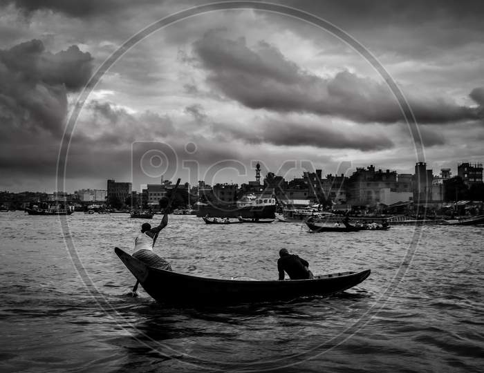 A Boatman And Passenger On The River Under Cloudy Sky .