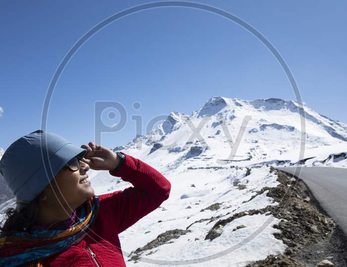 A Beautiful Young Lady With A Red Sweater, A Blue Cap And With Spectacle Enjoying Nature On A Snow Covered High Altitude Pass On Himalaya